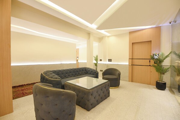 A modern waiting area with a sectional sofa, a round armchair, and a glass-top coffee table. - Fabhotel Ronald Inn (Faridabad)