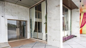 A modern building entrance with glass doors, a marble floor, and a tiled area with plants.