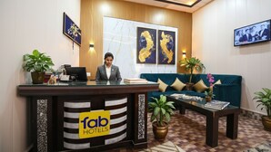 Ein Empfangstresen mit einem 'fab hotels' Schild, eine Rezeptionistin, ein blaues Sofa und mehrere Kübelpflanzen.