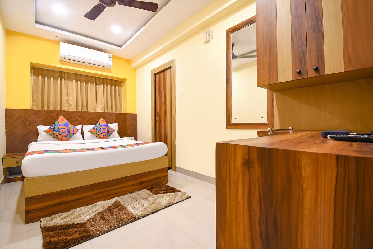 Un dormitorio con cama, cabecera de madera, escritorio con espejo y aire acondicionado.