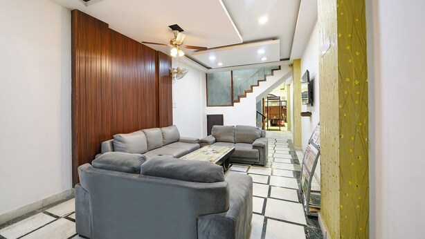 A modern living room with a grey sectional sofa, a ceiling fan, and a staircase leading to an upper level. - Fabhotel Delhi Darbar (New Delhi)
