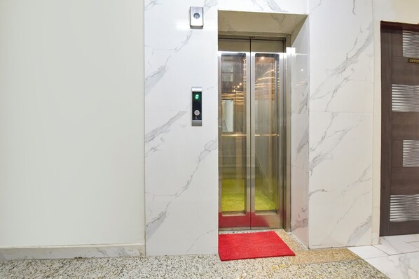 Un ascensor con pared de mármol, alfombra roja y panel de control digital.