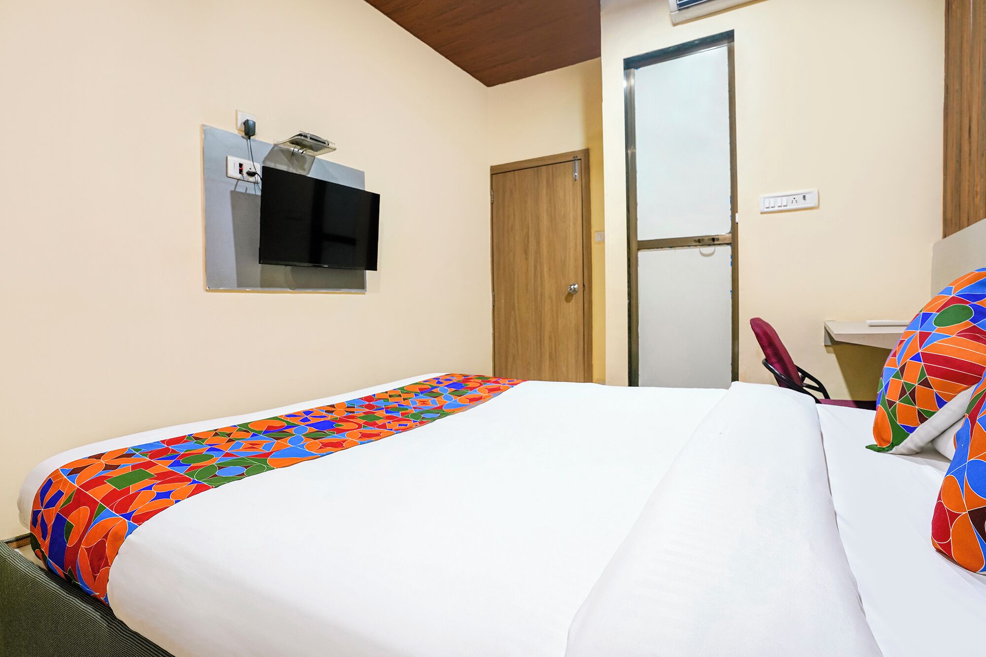 A hotel room with a bed, a television mounted on the wall, a door, and a small table with a chair.