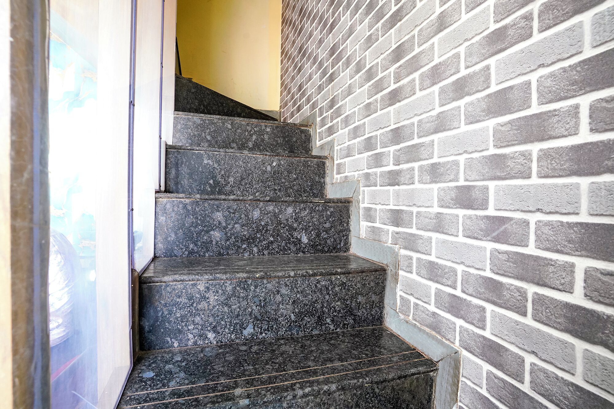 A staircase with dark granite steps leading up to a landing, adjacent to a brick wall.
