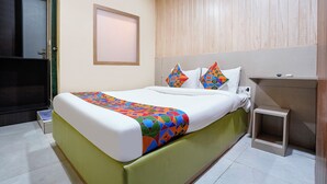 Ein Hotelzimmer mit Bett, einem kleinen Nachttisch, einem an der Wand befestigten Fernseher und einer Tür.