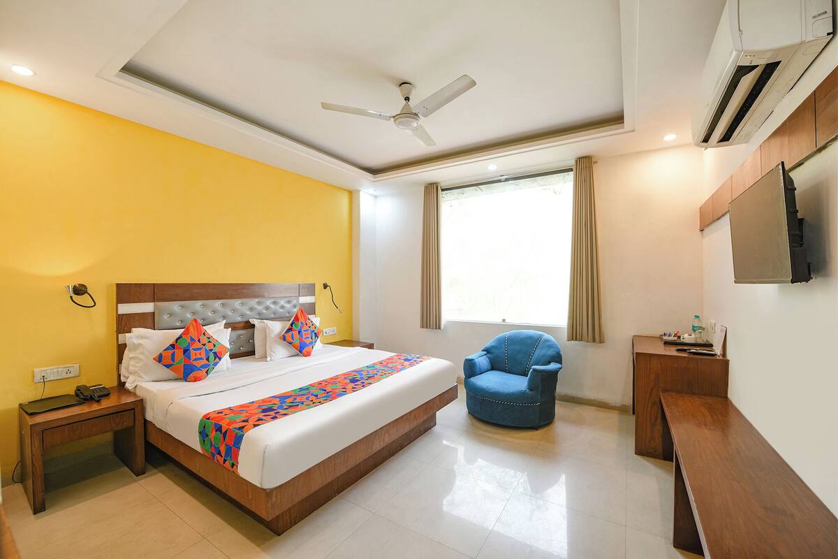 A hotel room with a bed, a chair, a desk, a ceiling fan, and a window with curtains.