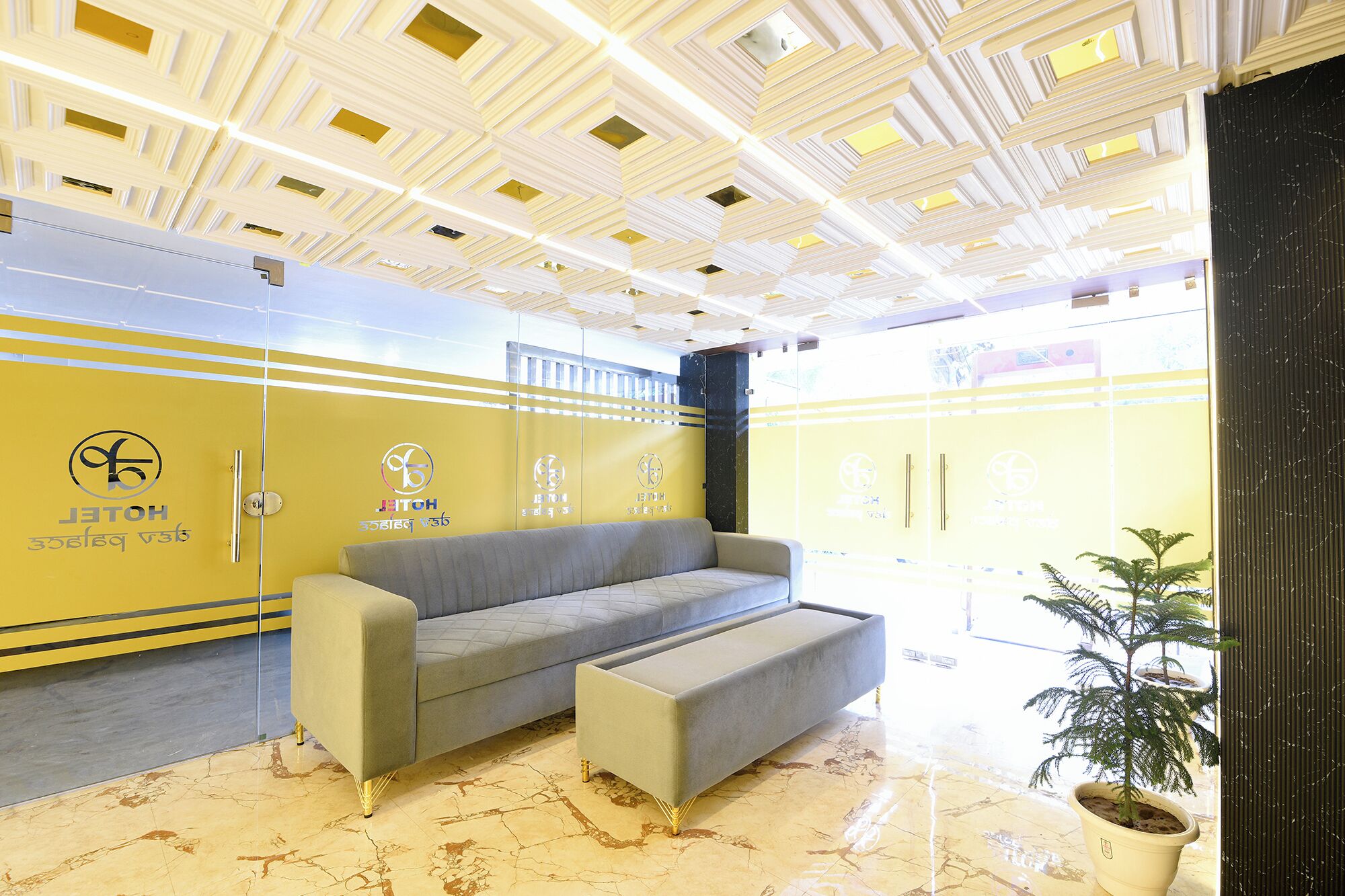 Un hall d’hôtel avec un canapé, une plante en pot et un plafond orné de motifs.