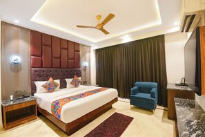 A hotel room with a large bed, a ceiling fan, a blue armchair, and a desk with a telephone. - FabHotel Dev Palace Naraina (New Delhi)