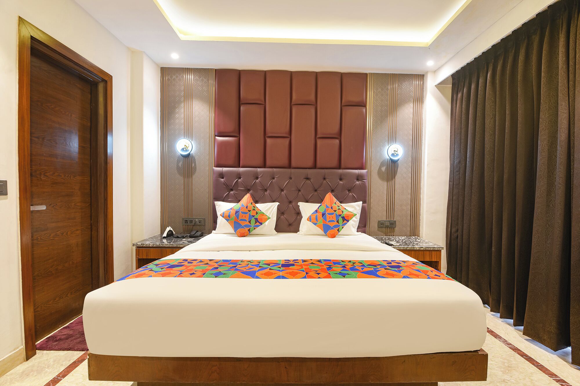 A hotel room with a large bed, two bedside tables, a wooden headboard, and a curtain on the right side.