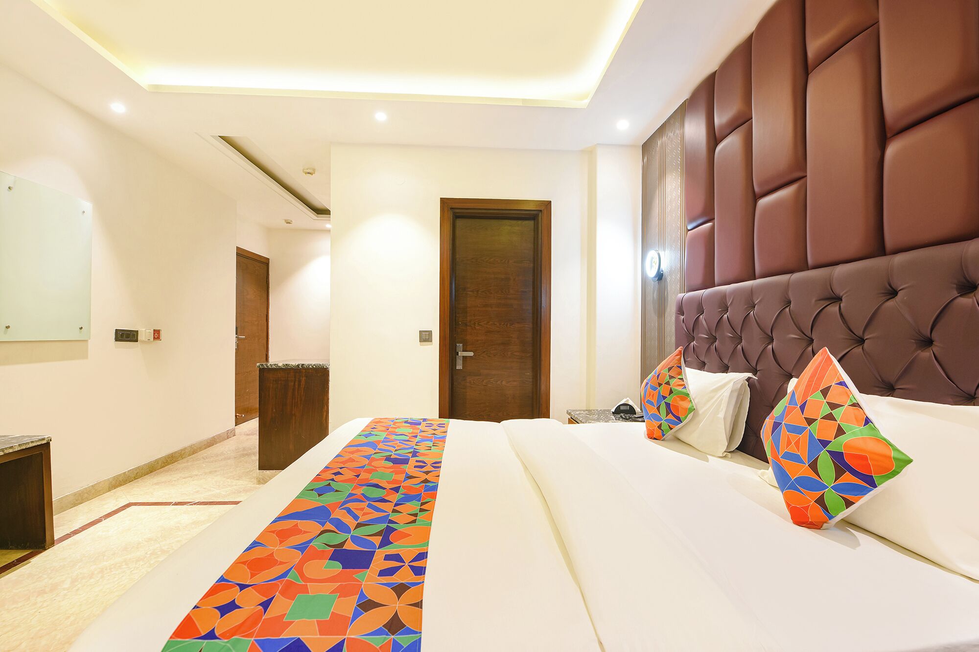Une chambre d’hôtel avec un lit, une tête de lit, une porte et un couloir.