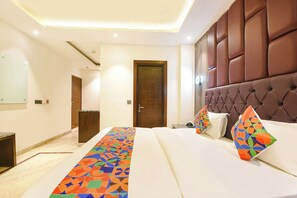 A hotel room with a bed, a headboard, a door, and a hallway. - FabHotel Dev Palace Naraina (New Delhi)