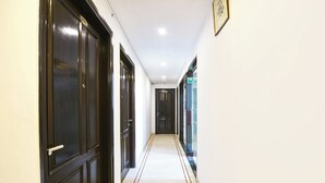 A corridor with dark wooden doors, a white tiled floor, and a fire exit sign. - Fabhotel Green Park (New Delhi)