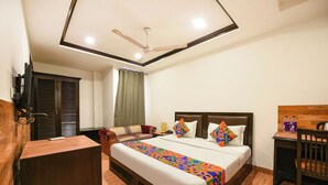 A hotel room with a large bed, a desk, a chair, a ceiling fan, and a window with curtains. - Fabhotel Green Park (New Delhi)