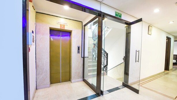 An elevator with a "Fire Exit" sign above it, a glass door, and a staircase with a metal railing. - Fabhotel Green Park (New Delhi)