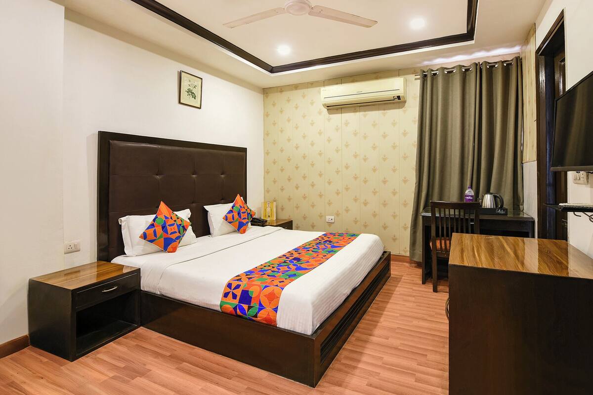 A hotel room with a bed, a desk, and an air conditioning unit.