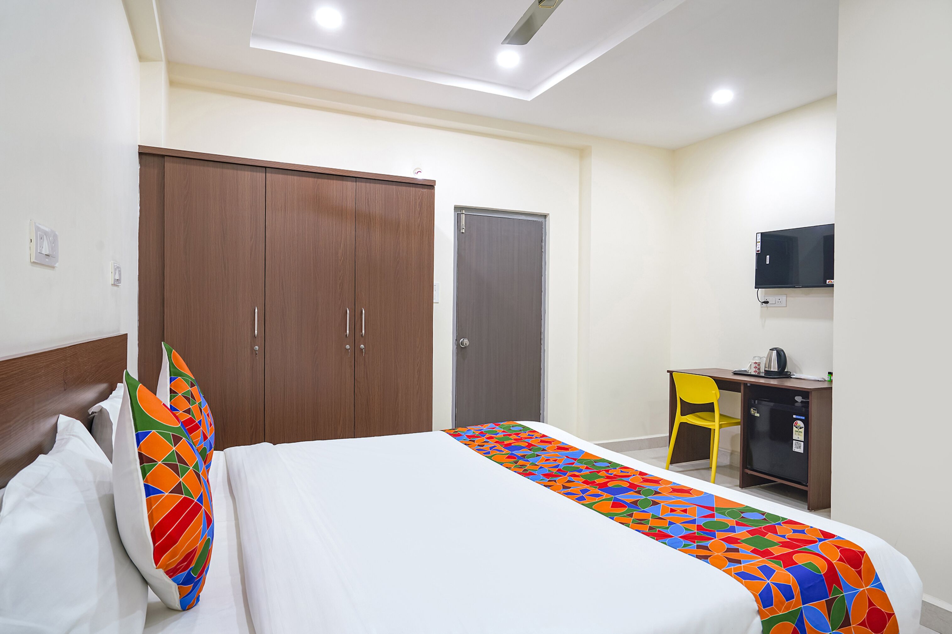 A hotel room with a bed, a wardrobe, a desk with a chair, and a television.