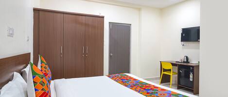A hotel room with a bed, a wardrobe, a desk with a chair, and a television.