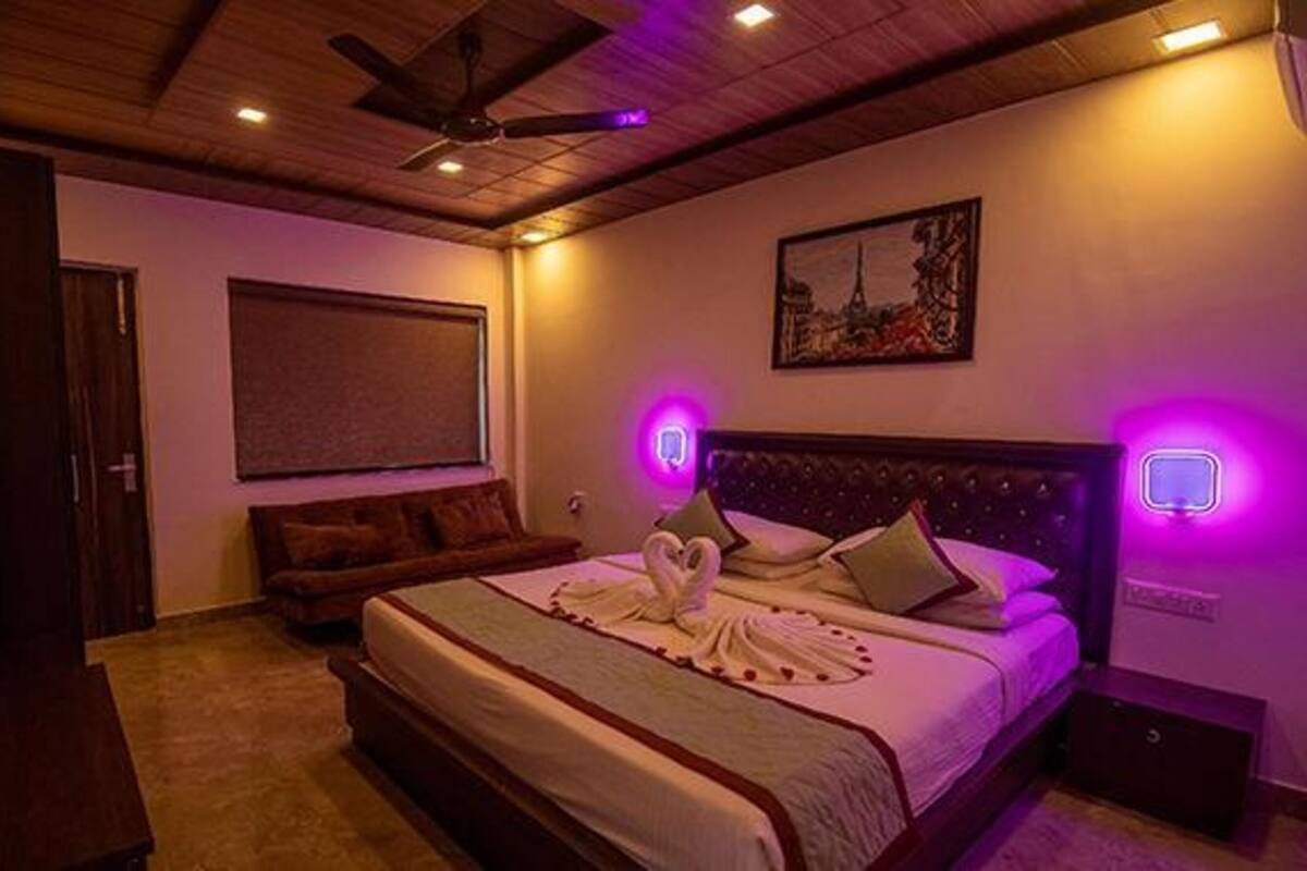 Ein Schlafzimmer mit einem Bett, einem Deckenventilator, einem Gemälde und einer violetten Leuchte.