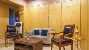 Ein Zimmer mit Wandpaneelen aus Holz, einem grauen Sofa mit blauen Kissen, zwei Holzsesseln, einem Holztisch und einer wandmontierten Klimaanlage.