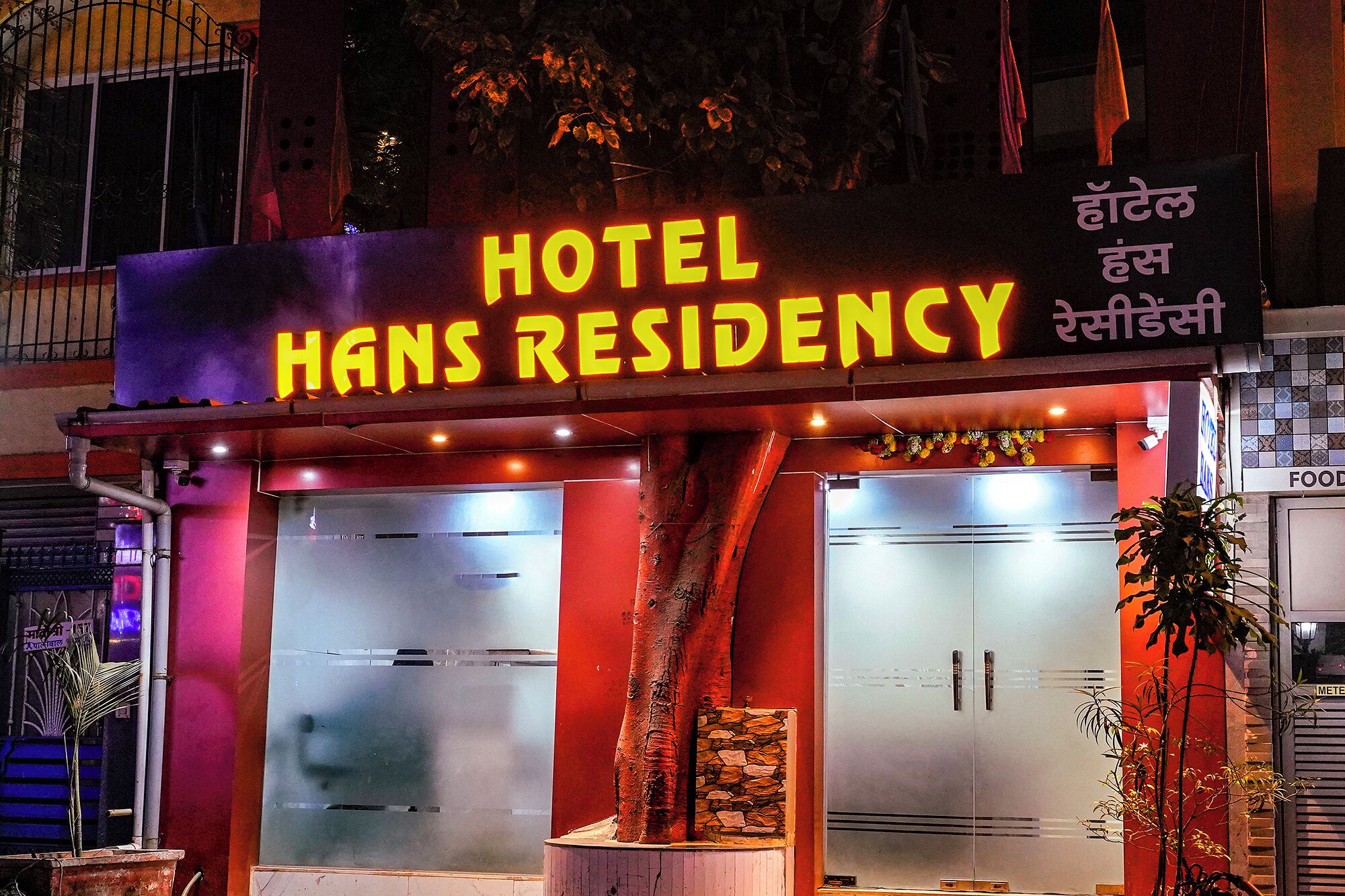 A hotel named "Hans Residency" with a neon sign, large glass doors, and a red facade.