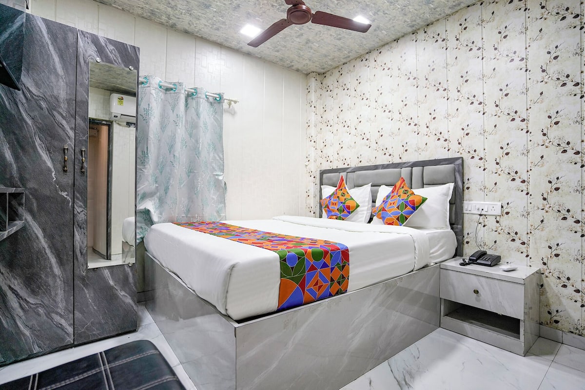 A modern bedroom with a marble wall, a bed with a colorful quilt, a nightstand with a phone, and a ceiling fan.