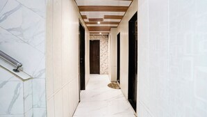 A hallway with white marble floors and walls, wooden ceiling beams, and a metal handrail on the left. - Fabhotel Hans Residency (Mumbai)