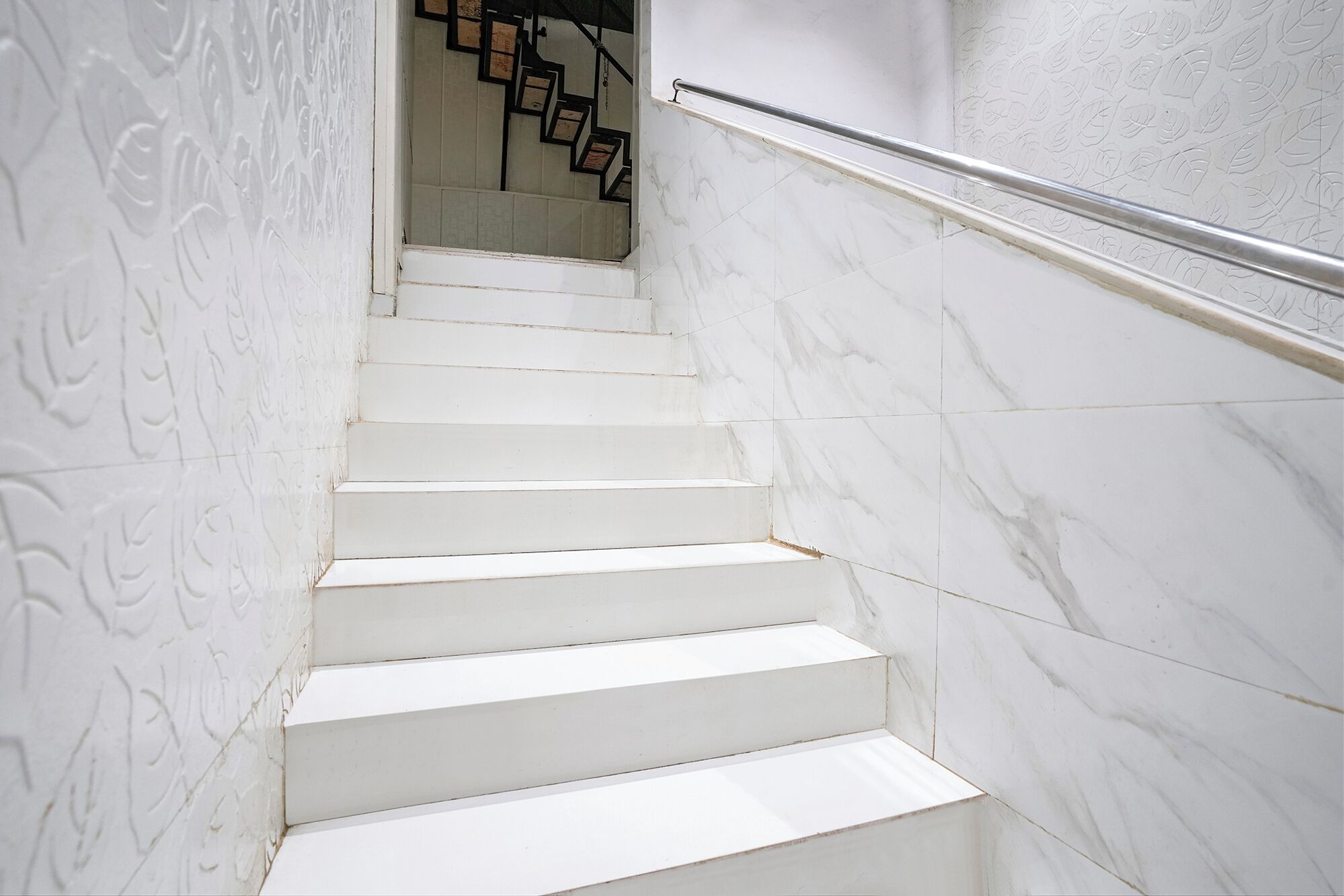 A white marble staircase with a metal handrail, leading to a landing with a black metal staircase.