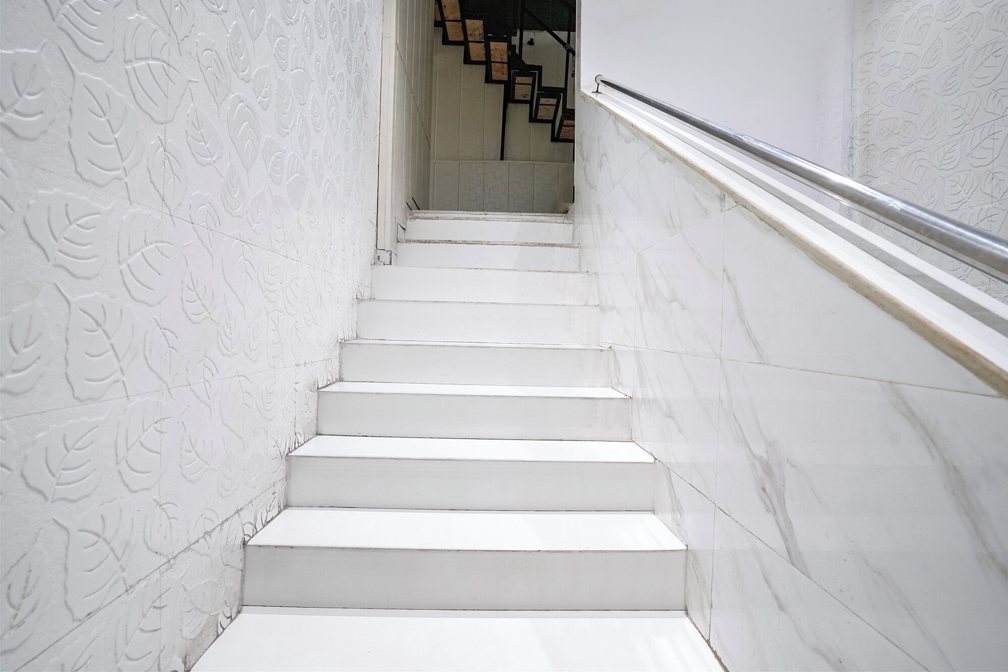 A white staircase with a railing, leading to a landing with a wooden staircase.