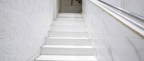 Una escalera blanca con barandilla que lleva a una plataforma con escalera de madera.