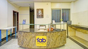 A reception desk at a hotel with a marble counter, glass railings, and a reception area with a window and blinds. - Fabhotel Aig Broholic (Hyderabad)