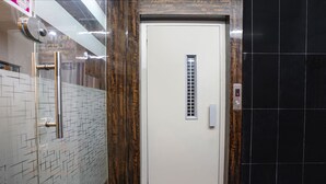 A hotel elevator with a white door, a control panel, and a black tiled wall. - FabHotel Alpine I - Inside Shivani Avenue (Ahmedabad)