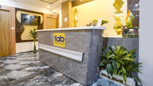 A hotel reception desk with a 'fab hotels' sign, a flat-screen TV, and a modern interior design. - FabHotel Alpine I - Inside Shivani Avenue (Ahmedabad)