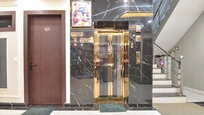 A modern elevator with marble walls, a wooden door, and a staircase with a metal railing. - Fabhotel Mahadev Palace (Haridwar)