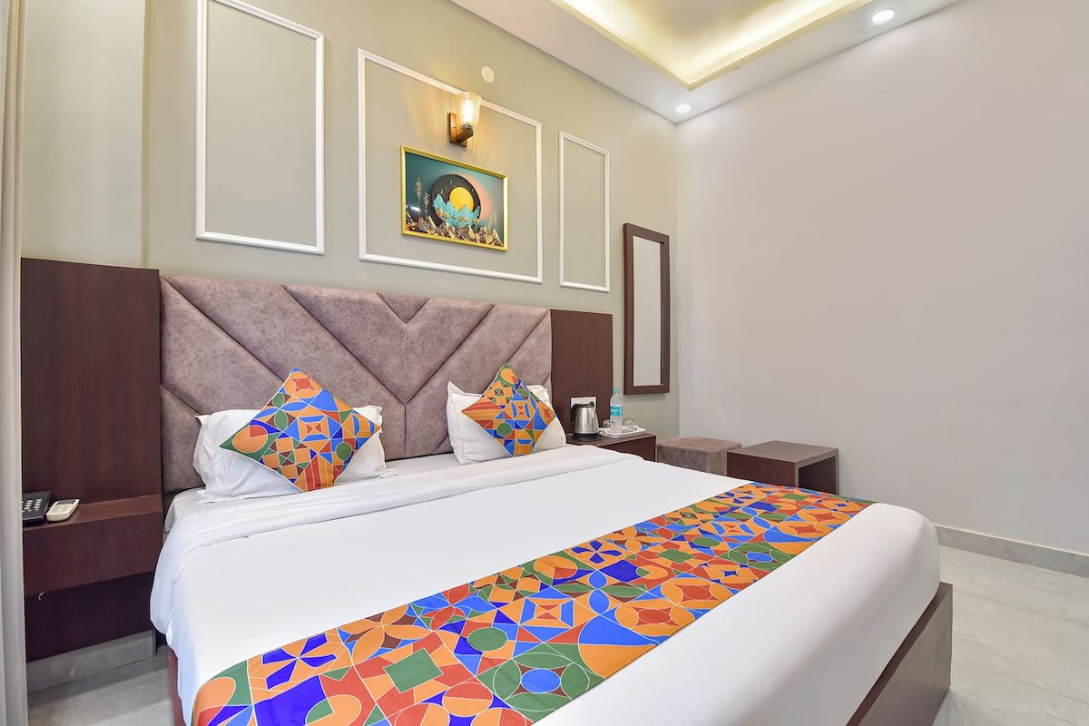 A hotel room with a large bed, a headboard, a nightstand, a bedside table, and a wall-mounted light fixture.