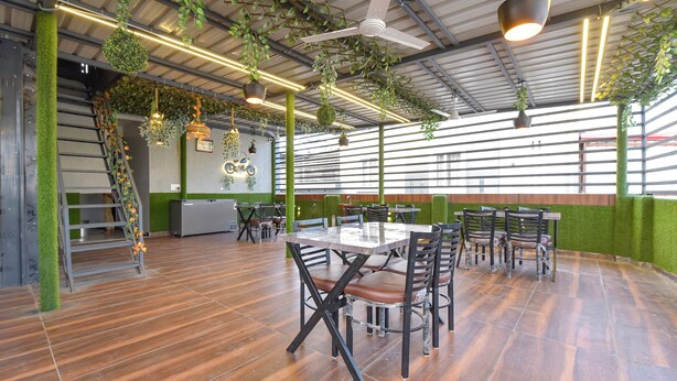 A spacious indoor area with wooden flooring, multiple tables and chairs, ceiling fans, and hanging plants. - Fabhotel Mahadev Palace (Haridwar)