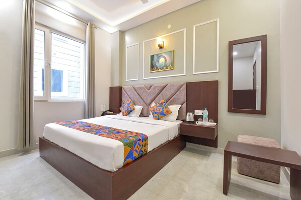 A hotel room with a large bed, bedside table, and a small seating area. - Fabhotel Mahadev Palace (Haridwar)