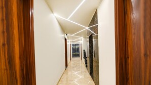 Un pasillo moderno con puertas de madera, suelo de mármol e iluminación de techo con diseños geométricos.