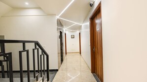 Un pasillo moderno con piso de mármol, barandales de metal negro y una puerta de madera al final.