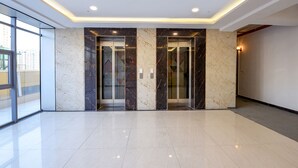 A modern lobby with marble walls, two elevators, and a large glass door leading outside. - FabHotel Prime Spectrum Metro - With Pool | 5 mins Walk from Sector 75 Metro (Noida)