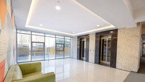 A spacious lobby with a modern design, featuring a seating area, a glass elevator, and a large window offering a view of the cityscape. - FabHotel Prime Spectrum Metro - With Pool | 5 mins Walk from Sector 75 Metro (Noida)