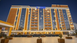 A multi-story hotel with a modern facade, large windows, and a well-lit entrance area with planters. - FabHotel Prime Spectrum Metro - With Pool | 5 mins Walk from Sector 75 Metro (Noida)