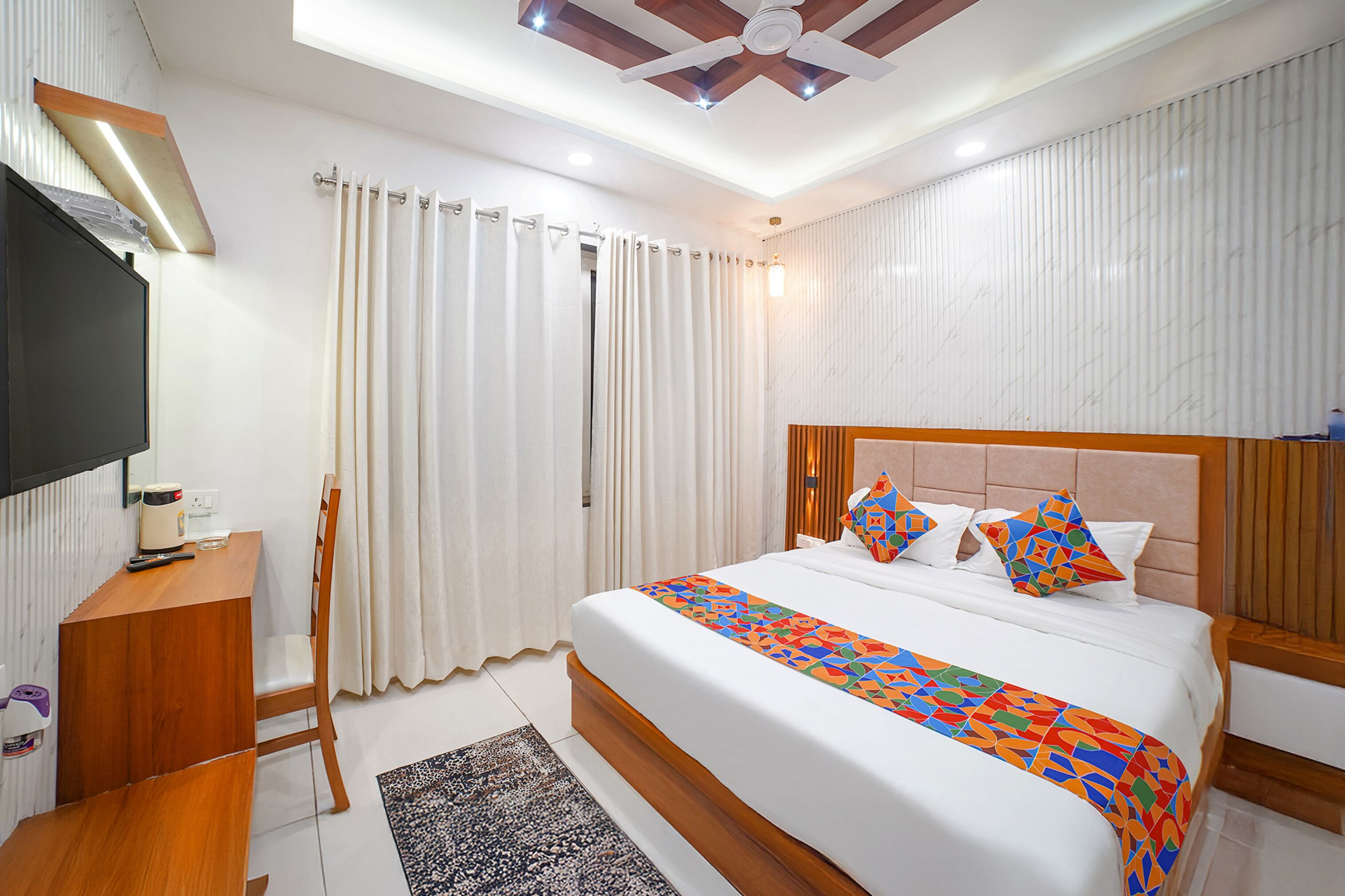 Une chambre d’hôtel moderne dotée d’un grand lit, d’une table de chevet en bois, d’un téléviseur à écran plat et d’un ventilateur de plafond.
