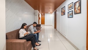 A hallway with a brown bench, white walls, and framed artwork on the right. - Fabhotel Eminent (Bhopal)