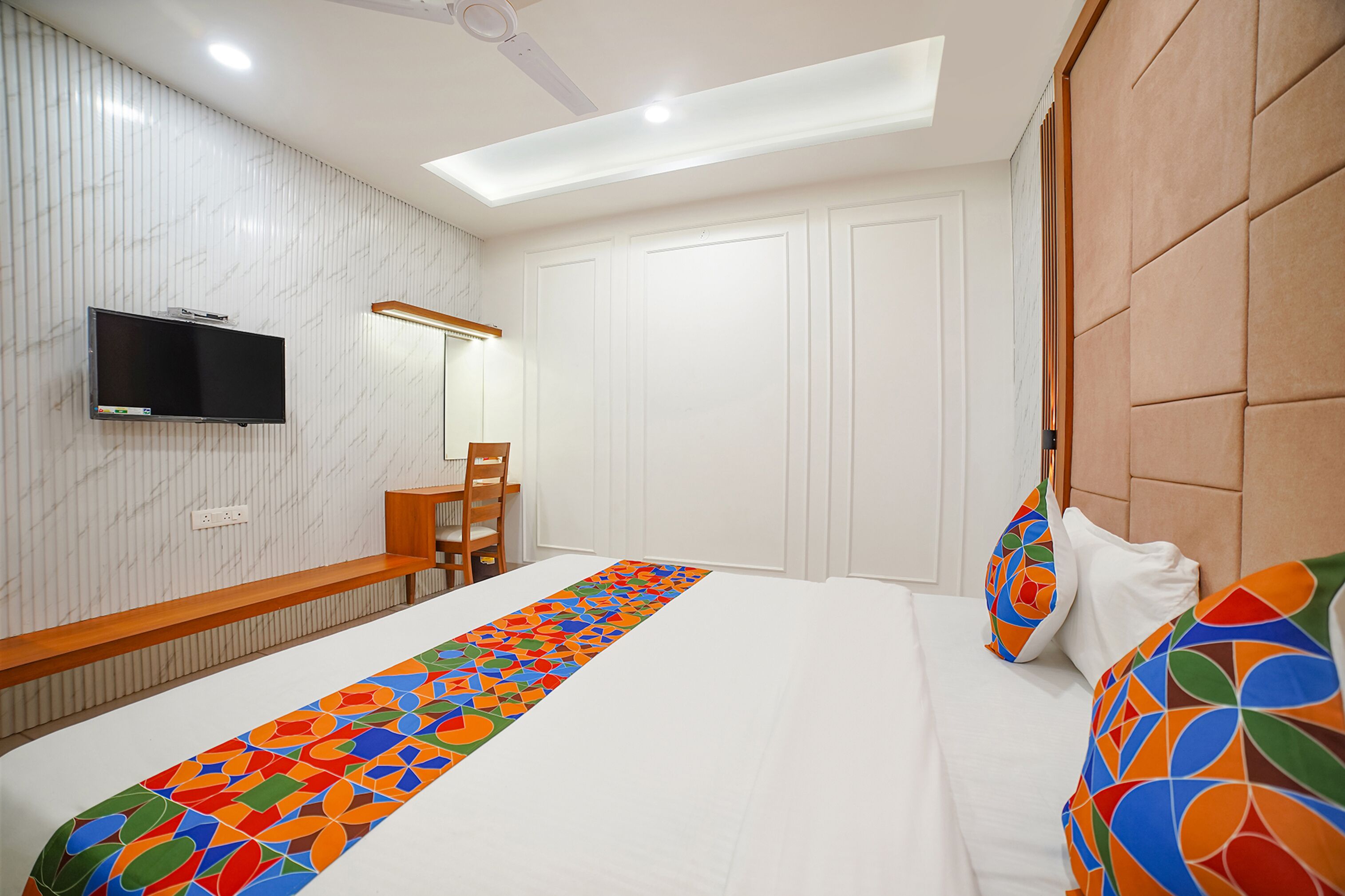 A hotel room with a bed, a desk, a chair, a television, and a patterned runner.