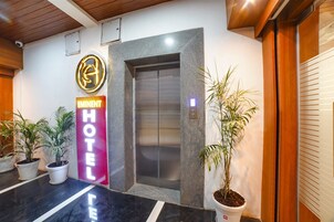 An elevator with a modern design, a prominent hotel sign, and potted plants near the entrance.
