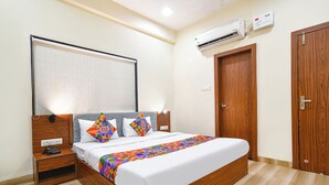 A hotel room with a wooden bed, a bedside table with a phone, a wall-mounted air conditioner, and a wooden wardrobe. - Fabhotel Weekend (Indore)