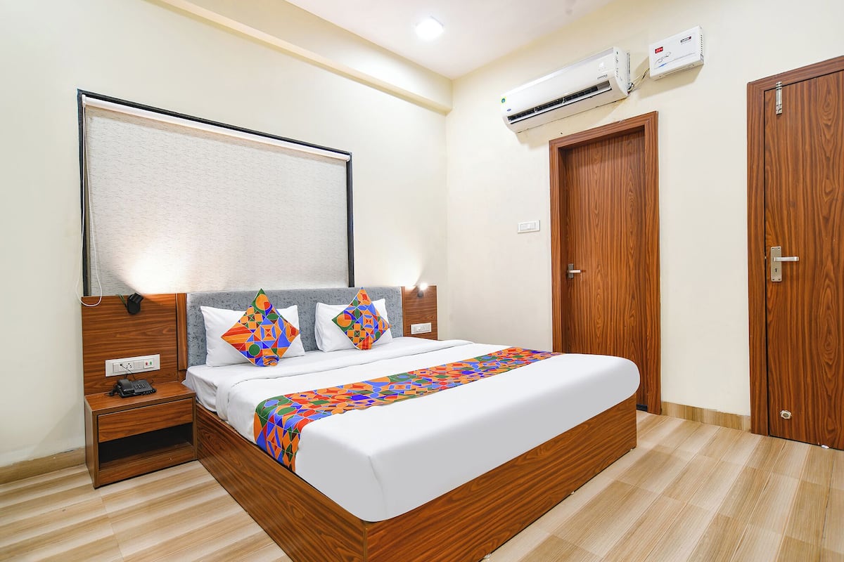 Habitación de hotel con cama de madera, mesita de noche con teléfono, aire acondicionado de pared y armario de madera.