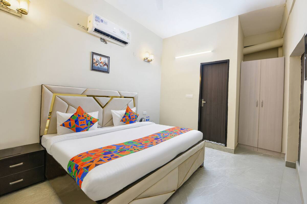 A hotel room with a large bed, a bedside table, an air conditioning unit, a wardrobe, and a door.