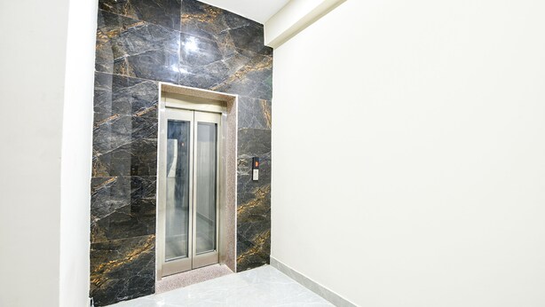 Een hal met een marmeren muur en een glazen liftdeur.