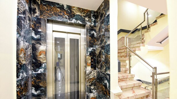 An elevator with marble walls and a digital display, next to a staircase with metal railings and marble steps.